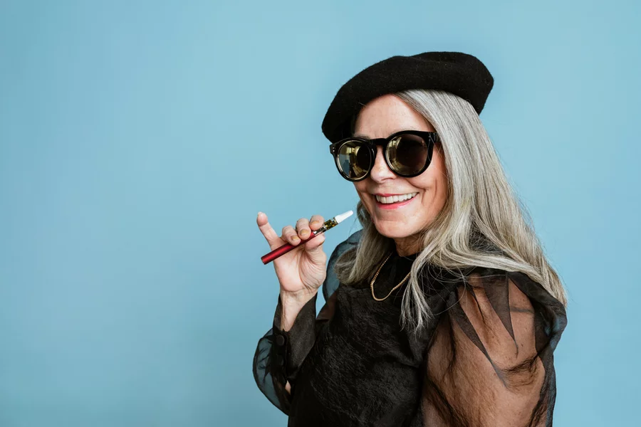 A mature woman holds her vape pen in front of a blue background.