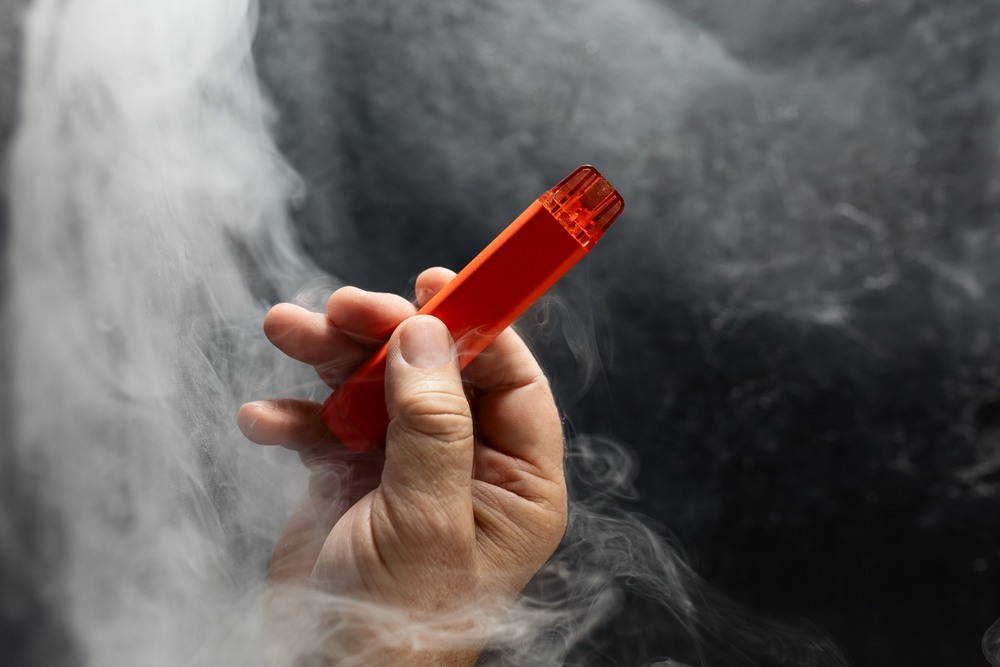 A hand holds a vape pen, surrounded by a cloud of vapor. 