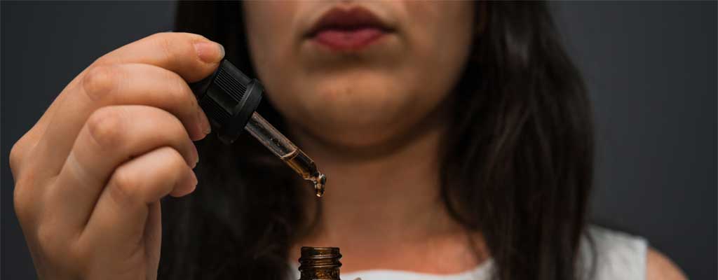 A woman holds up a dropper of CBD oil
