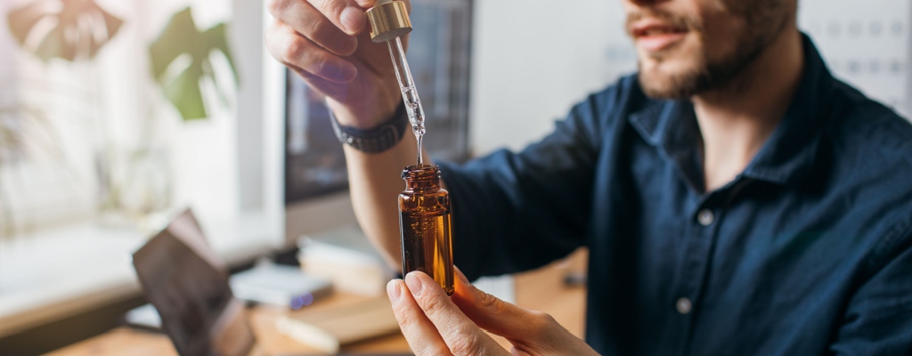 A man prepares a dose of CBD oil while sitting at his desk.