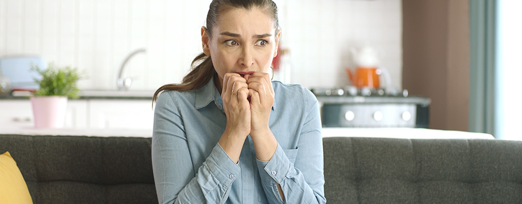 An upset woman sits on a couch in her home.