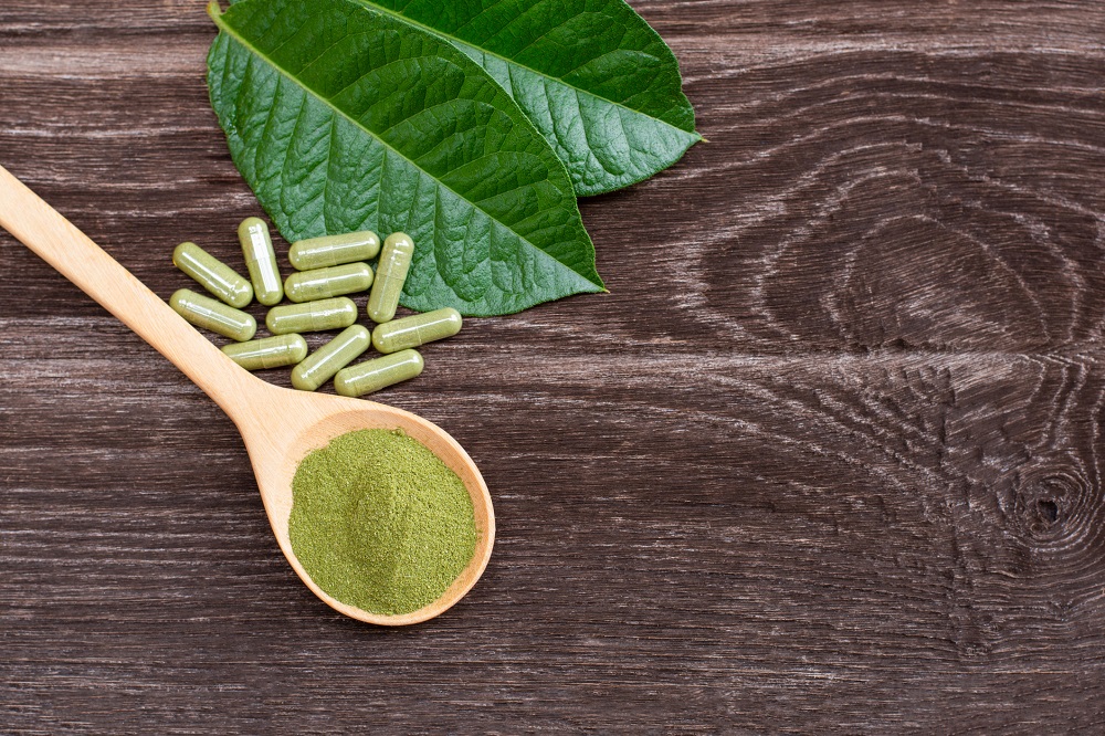 kratom leaf (mitragyna speciosa) with kratom powder capsule isolated on wooden table background.