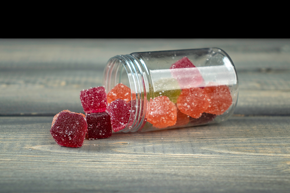 A jar of CBD gummies open on its side, sitting on a wooden table.