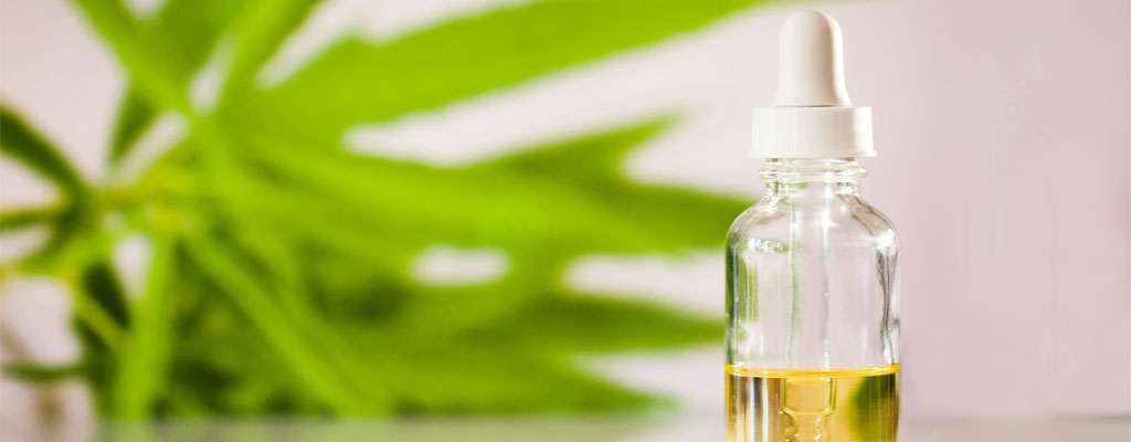 A bottle filled with CBD oil sits on a table with a hemp leaf in the background.