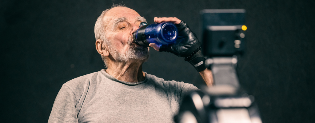 A man exercises on a stationary bike while drinking water.