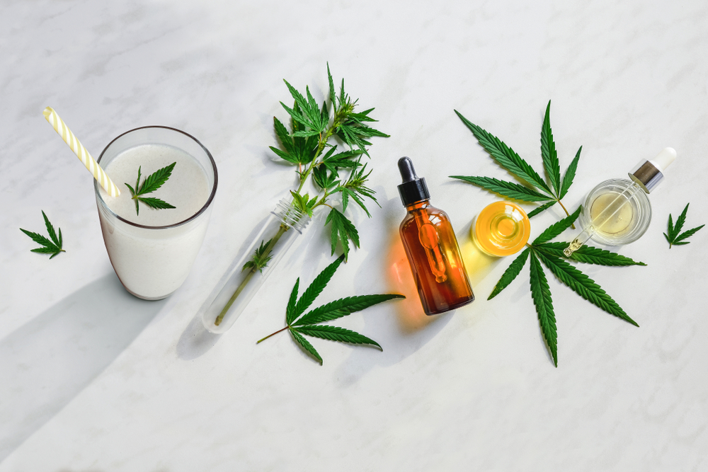 CBD products and hemp leaves sit on a white stone table.