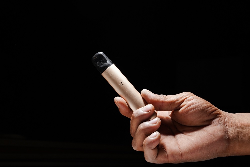 A hand holds a vape pen in front of a black background.