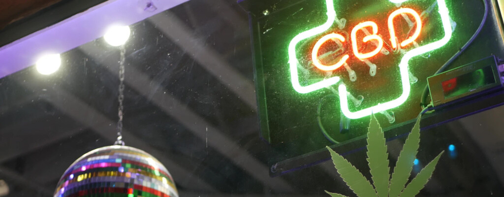 A neon sign reading "CBD" hangs in a smoke shop window.