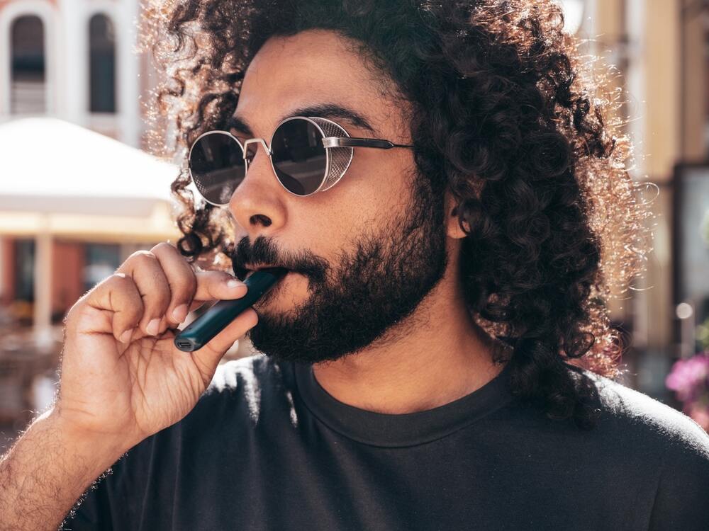 A man uses a disposable vape outdoors.