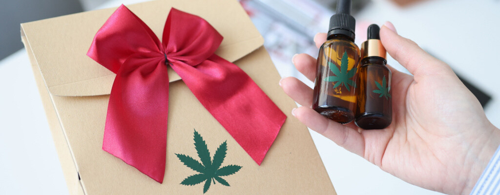 Hands hold 420-inspired gifts, including oils and tinctures.