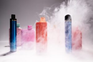 Several disposable vapes sit surrounded by a cloud of vapor. 