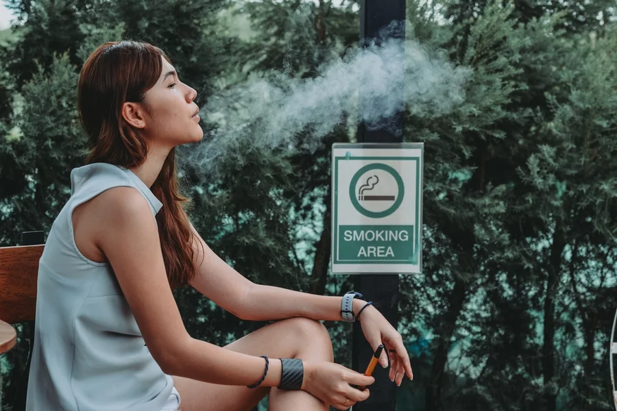 A woman enjoys a vape while seated in a smoking area.