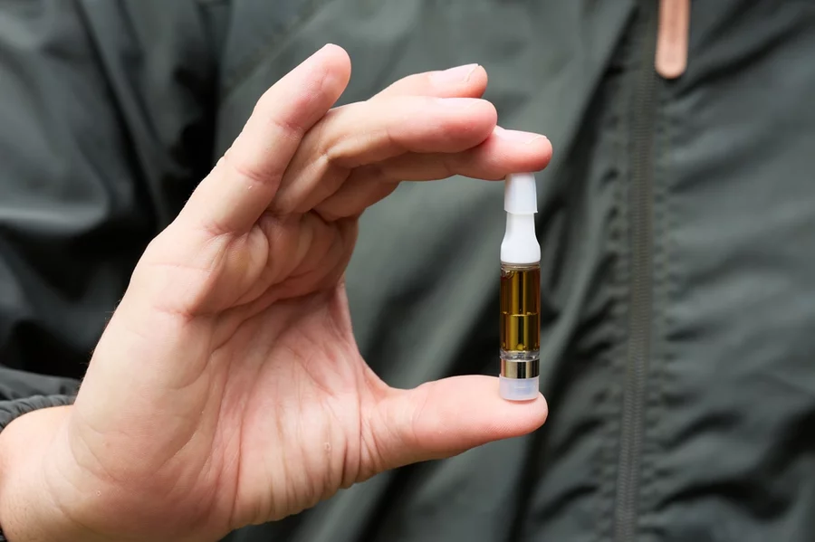 A man holds a CBD vape cart between his thumb and forefinger.