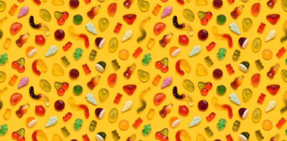 A variety of gummy candies sit on a yellow background. 