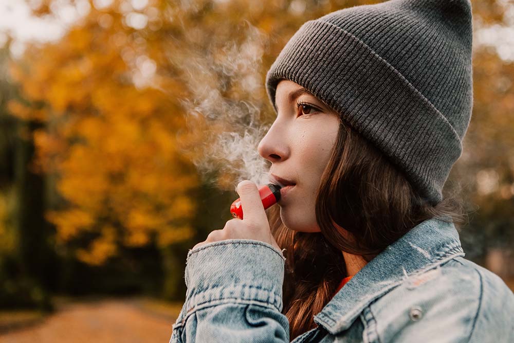 A young woman uses a vape in a park