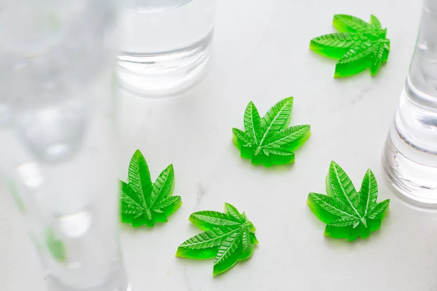 Green hemp leaf-shaped gummies sit on a white table.