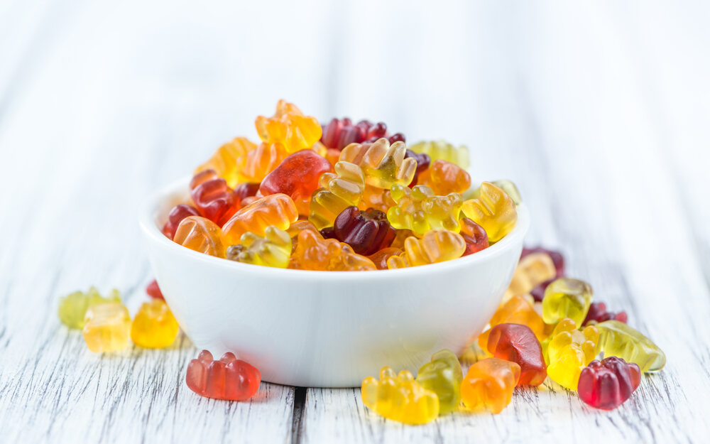 Gummy bears sit in a white bowl on a white table.