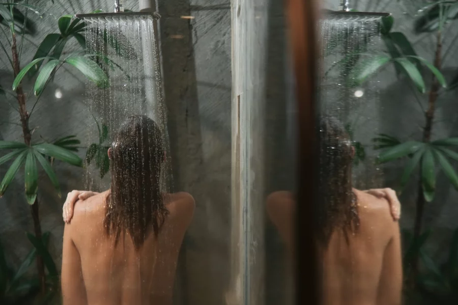 A woman showers in a large, dark walk-in glass shower.