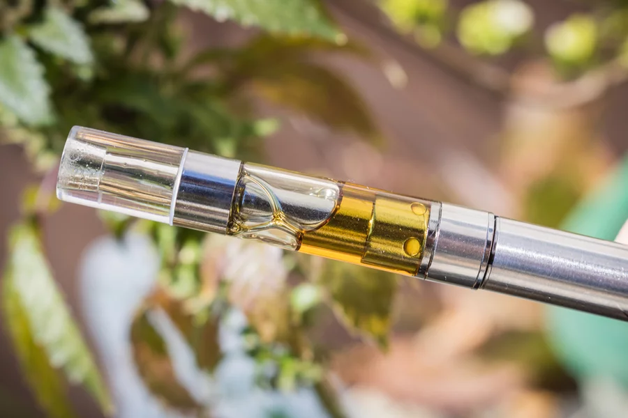 A close-up view of a vape cart filled with concentrate attached to a vape pen.