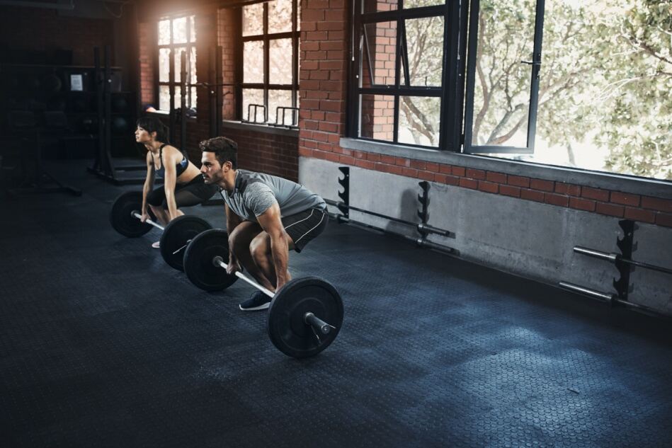 A man and woman complete deadlifts in a gym.