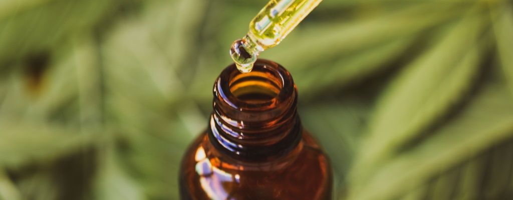 A dropper dispenses a drop of CBD oil back into the brown glass bottle in which it is housed. 