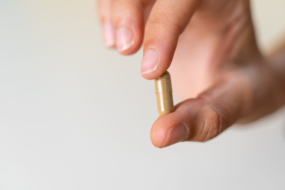 A hand holds a single mushroom capsule against a white background.