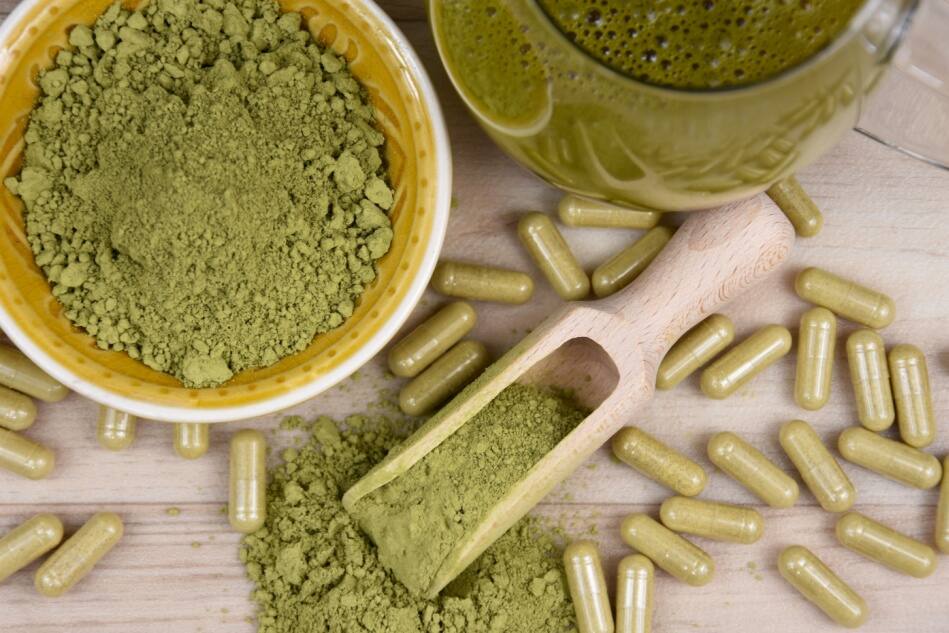 Kratom powder and capsules sit on a wooden table.