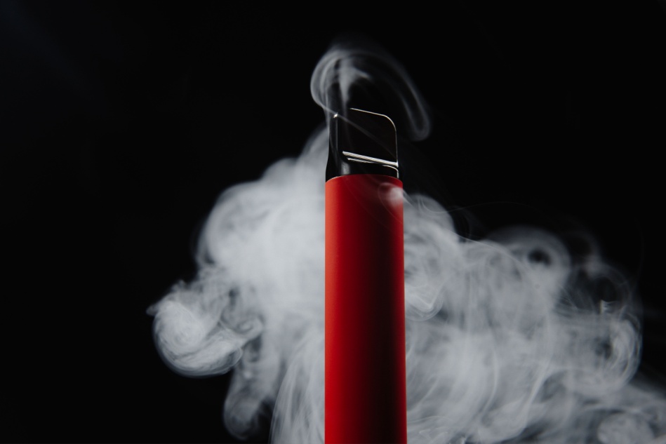 A disposable vape seen in front of a cloud of vapor and a black background.