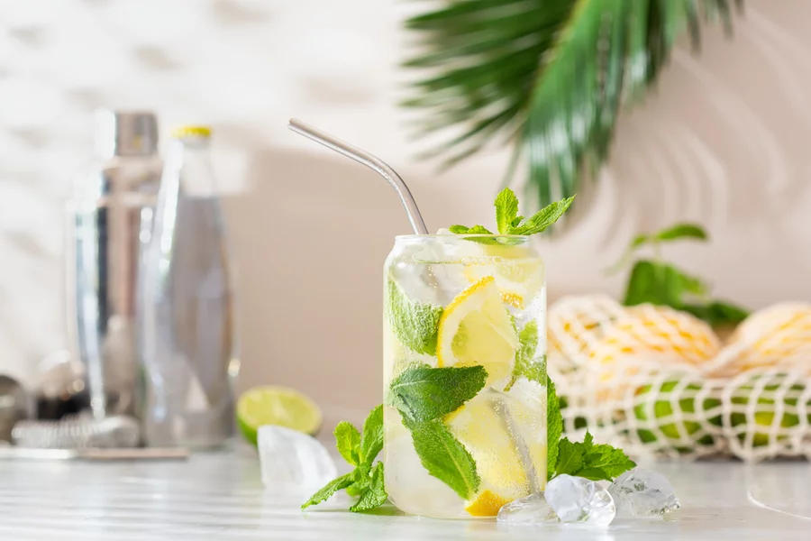 A THC seltzer served in a can-shaped glass with a metal straw, lemon, and mint.