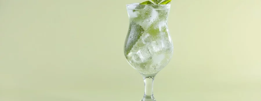 A glass of seltzer with ice and mint seen against a green background.