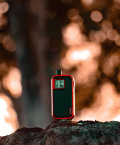 Image showing the difference between Delta-8 Edibles vs Vape showing a red and black vape displayed on top of a rock with a tree on the background.