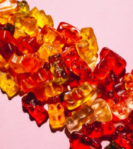 Image showing the difference between Delta-8 Edibles vs vape showing a pile of spilled orange and red gummies on pink background.