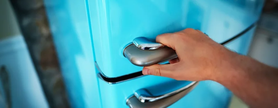 A man opens the freezer section of a blue refrigerator.