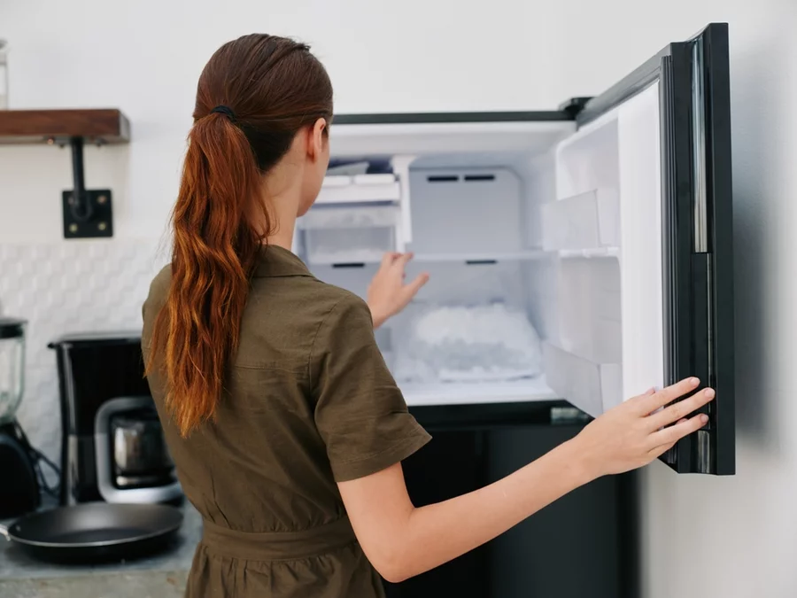 A woman opens a freezer in her kitchen.