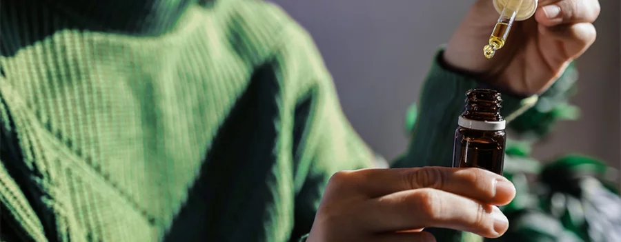 A woman holds a hemp oil dropper above its bottle before using it.