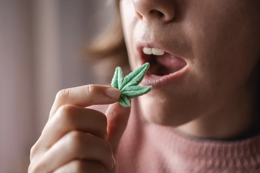 A woman eats an edible gummy shaped like a hemp leaf.