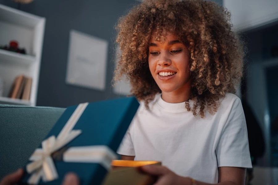 A young woman opens a wellness gift in a blue box.
