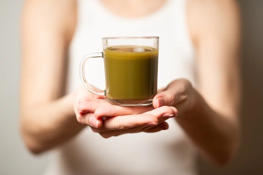 A woman holds a drink made from powdered kratom in a clear glass.