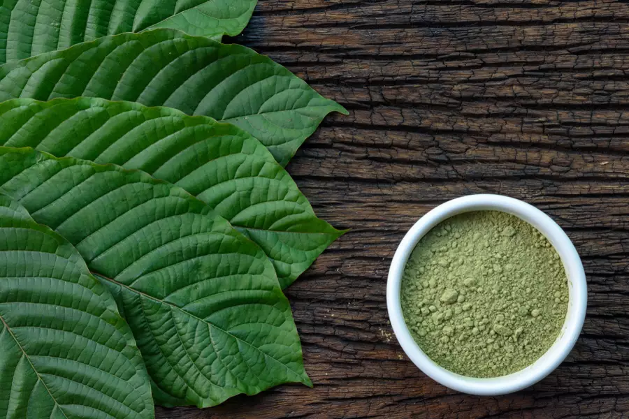 Kratom leaves and powdered kratom in a bowl seen from above on a wooden table.