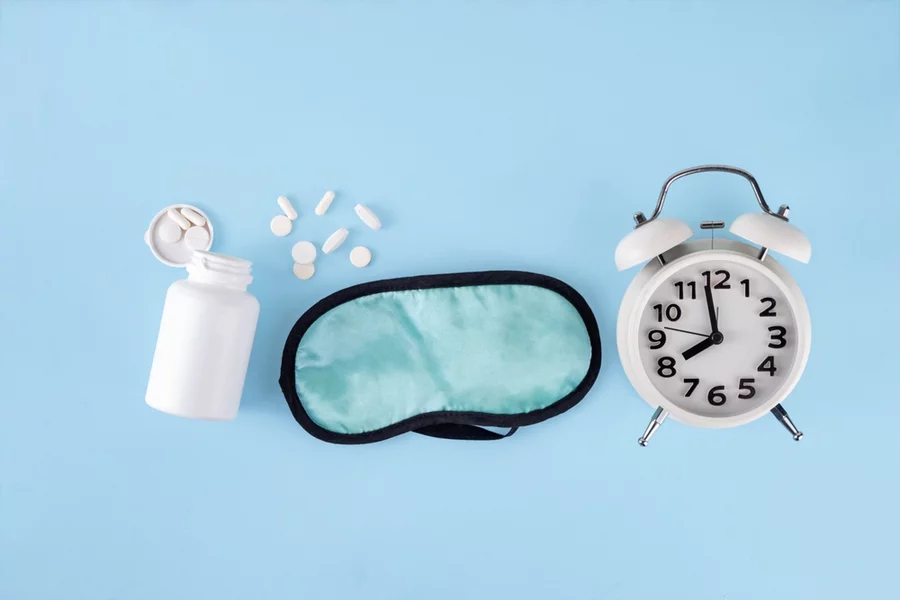 Sleep supplements, a sleep mask, and an alarm clock on a light blue background.