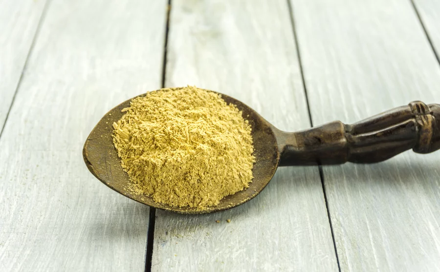 An ornate spoon with kava powder in its bowl sits on a table.