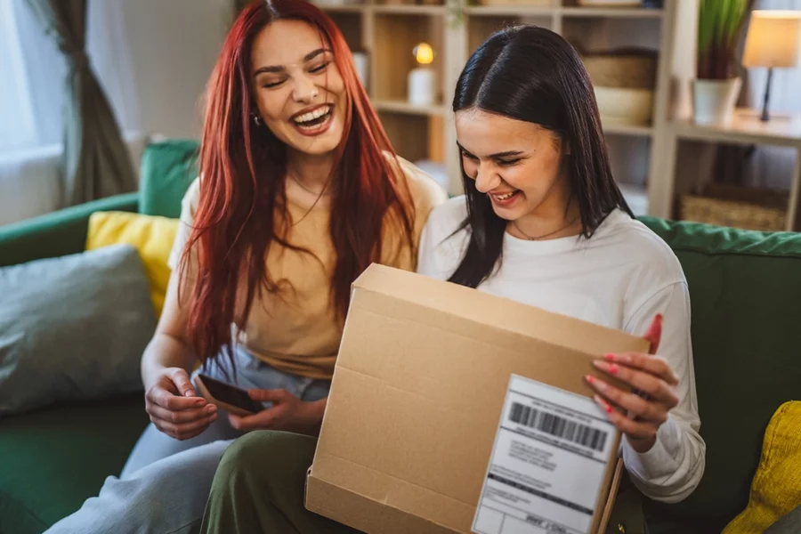 Two friends opening a calming wellness gift on a sofa.